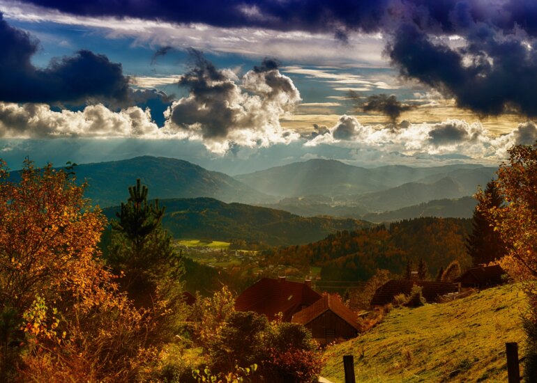 Landschaftsbild aus Kärnten, Österreich mit dramatischen Wolken, bewaldeten Hügeln und einer kleinen Hütte im Vordergrund