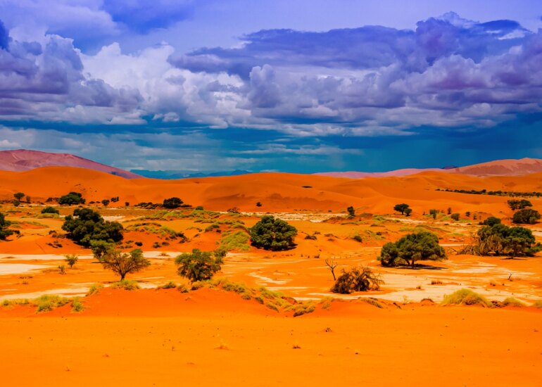 Dramatische Dünenlandschaft in Namibia mit leuchtend orangefarbenem Sand und Wolken am Himmel