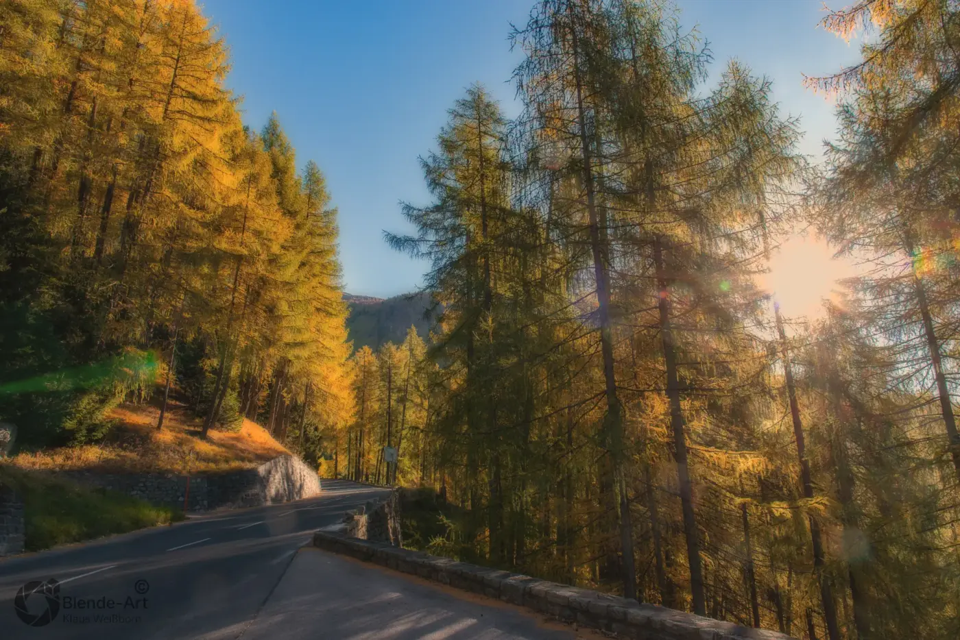 Herbstliche Bergstraße in Österreich mit goldenem Lärchenwald und Sonnenlicht, entlang der Nockalmstraße