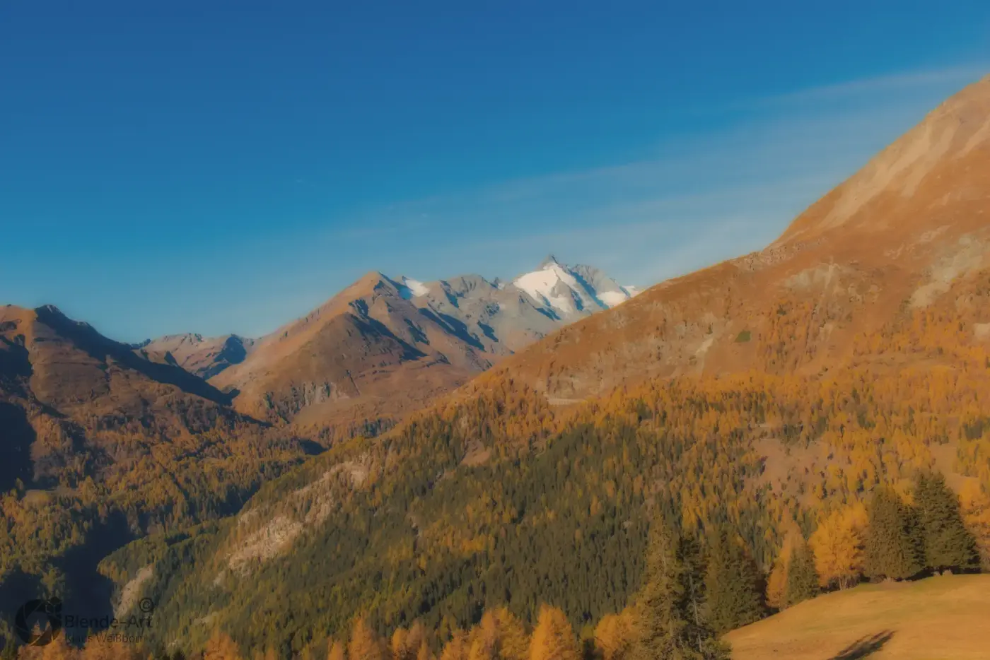 Herbstlandschaft in den österreichischen Alpen mit goldgelben Lärchenwäldern und einem schneebedeckten Gipfel im Hintergrund