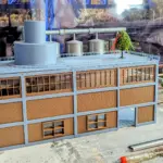 Modell-Lokschuppen mit montiertem Lüfterkamin und großem Abluftrohr, Richtbaum auf dem Dach sichtbar