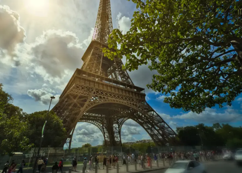 Eiffelturm in Paris im Gegenlicht der Sonne mit dramatischem Himmel und grünen Bäumen
