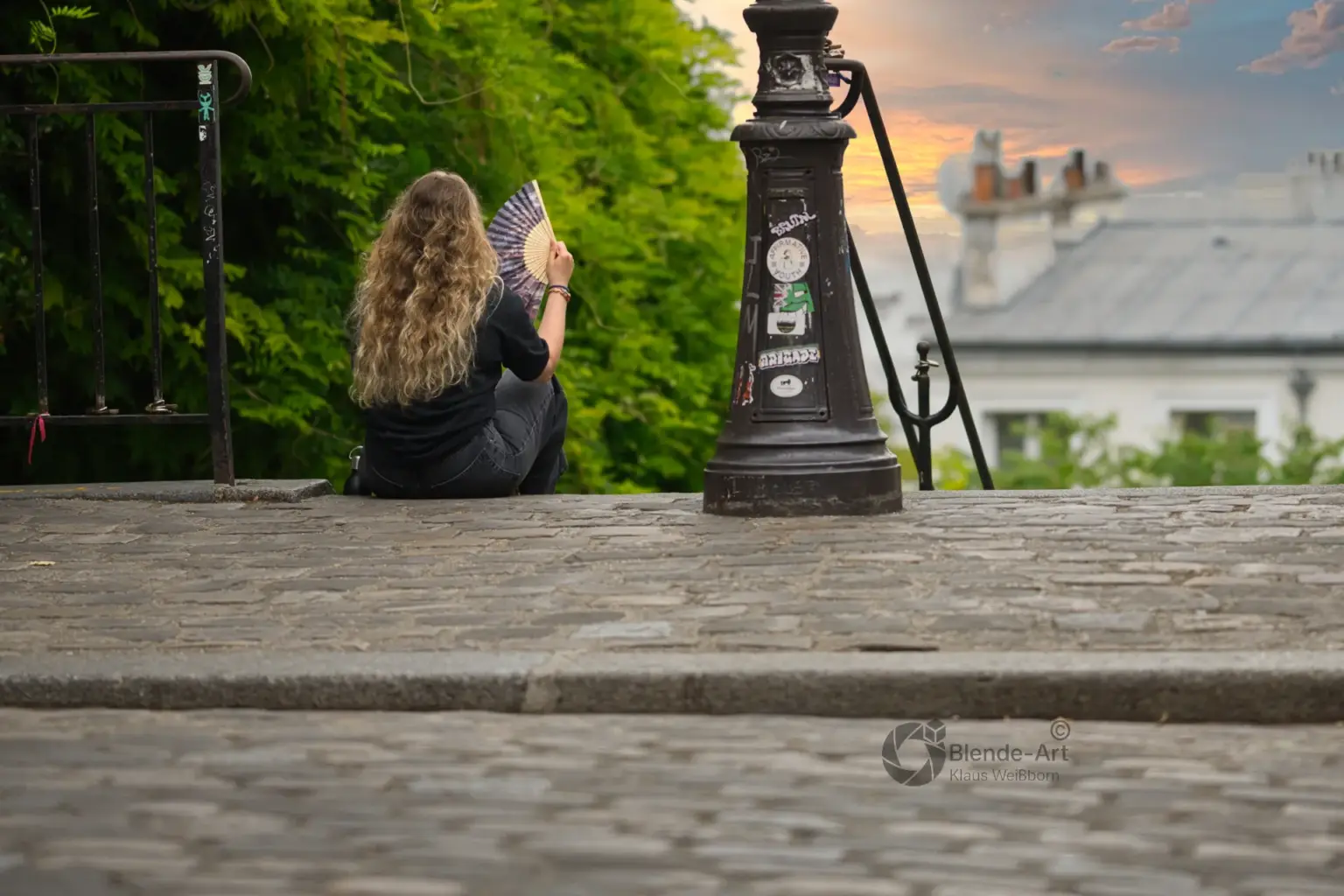 Person sitzt auf Kopfsteinpflaster mit Fächer in der Hand, geteilt in zwei Lichtstimmungen – links neutrales Tageslicht, rechts warmes Abendlicht. Zeigt den Unterschied zwischen hartem und weichem Licht.