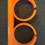 Frontansicht einer orangefarbenen 3D-gedruckten Dremel Doppelhalterung aus PETG, mit zwei kreisförmigen Aufnahmen und schmalem elastischem Spalt zur Klemmung.