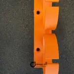 Seitenansicht einer orangefarbenen 3D-gedruckten Doppelhalterung aus PETG mit zwei Bohrungen zur Wandmontage, auf dunkler Unterlage fotografiert.