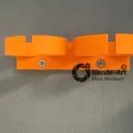 3D-gedruckte orangefarbene Dremel Halterung aus PETG, an einer grauen Wand montiert, mit zwei Schrauben befestigt.