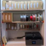 Schrank mit 3D-gedruckten Filamentrollenhaltern und Rundholzstangen zur übersichtlichen Aufbewahrung von 3D-Druck Filamentrollen