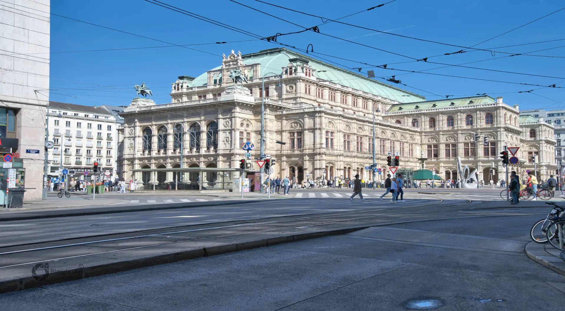 Panorama-Ansicht der Wiener Staatsoper am Opernring mit ihrer charakteristischen Neorenaissance-Fassade unter strahlend blauem Himmel.