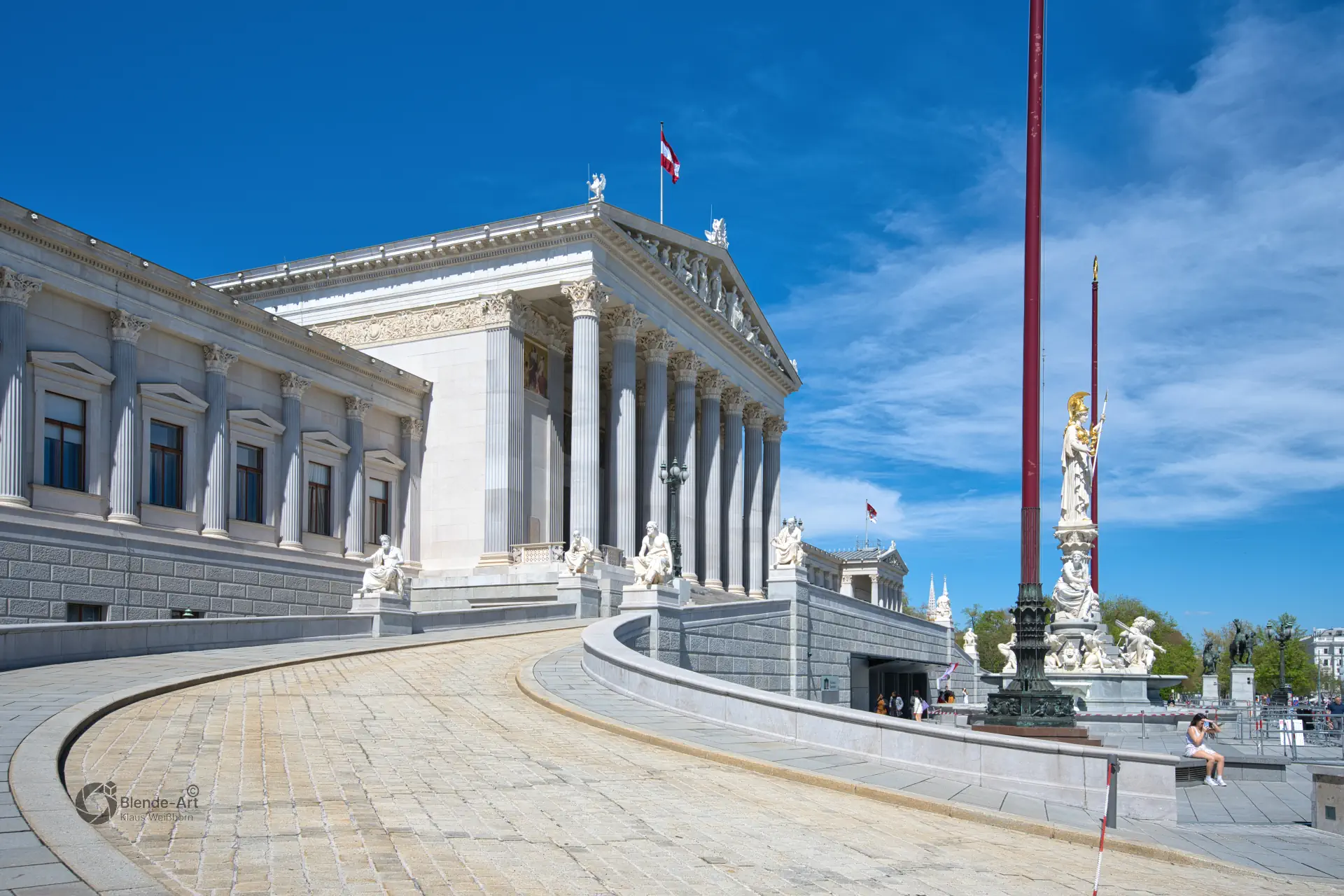 Panorama des Wiener Parlamentsgebäudes mit dem Pallas-Athene-Brunnen und der klassischen Säulenfassade unter strahlend blauem Himmel.