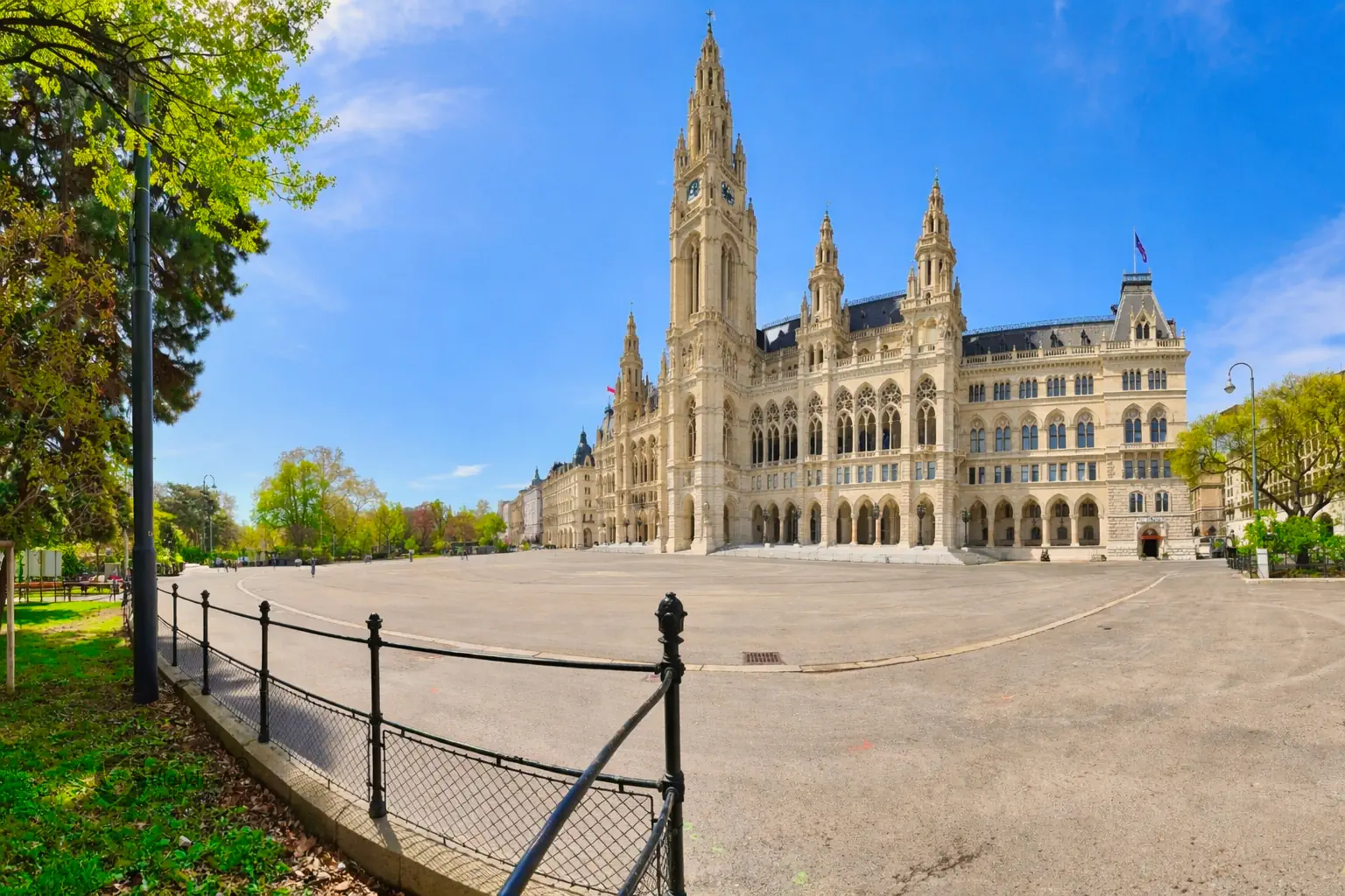Panorama des Wiener Rathauses mit seinem hohen Turm und der neugotischen Fassade unter strahlend blauem Himmel, eingerahmt vom Grün des Rathausparks.