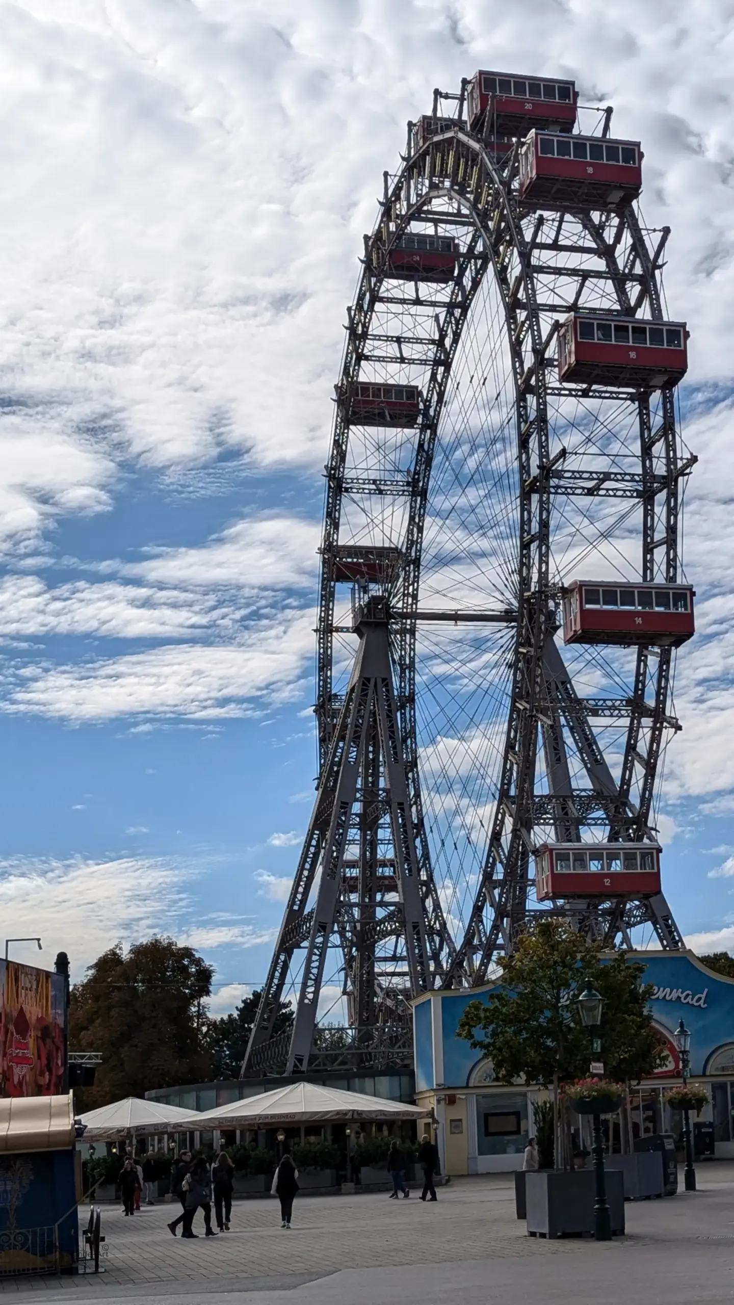 Nahaufnahme des historischen Wiener Riesenrads im Prater mit seinen charakteristischen roten Waggons gegen einen leicht bewölkten blauen Himmel.