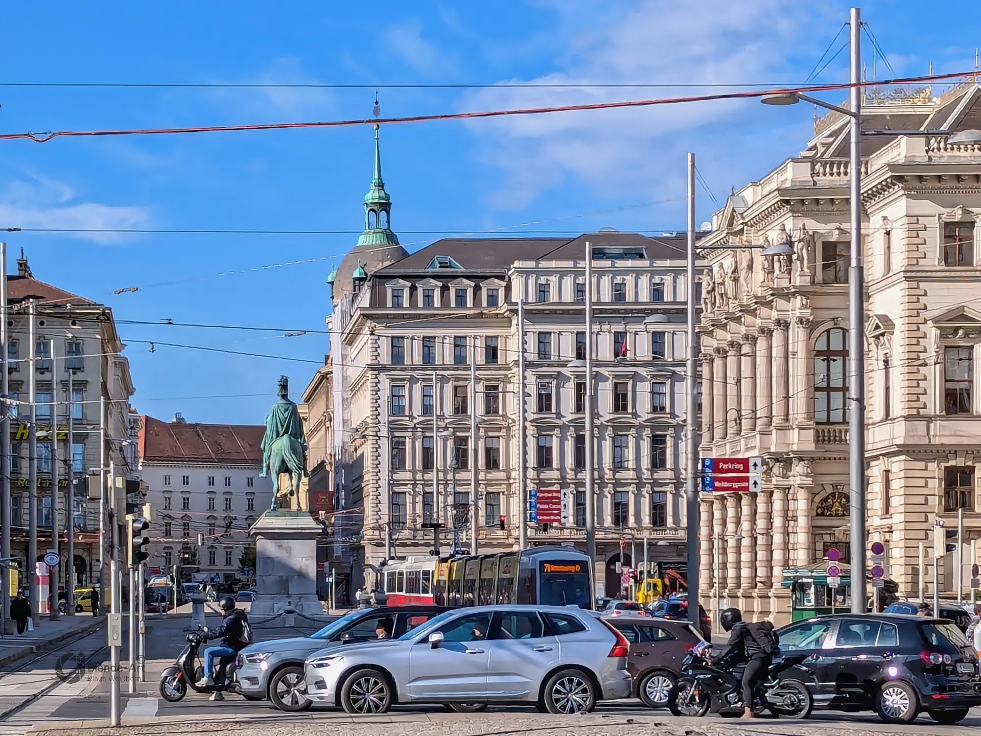 Blick über den Universitätsring auf das historische Palais Ephrussi am Schottentor mit einer modernen Straßenbahn und Passanten bei Tageslicht.