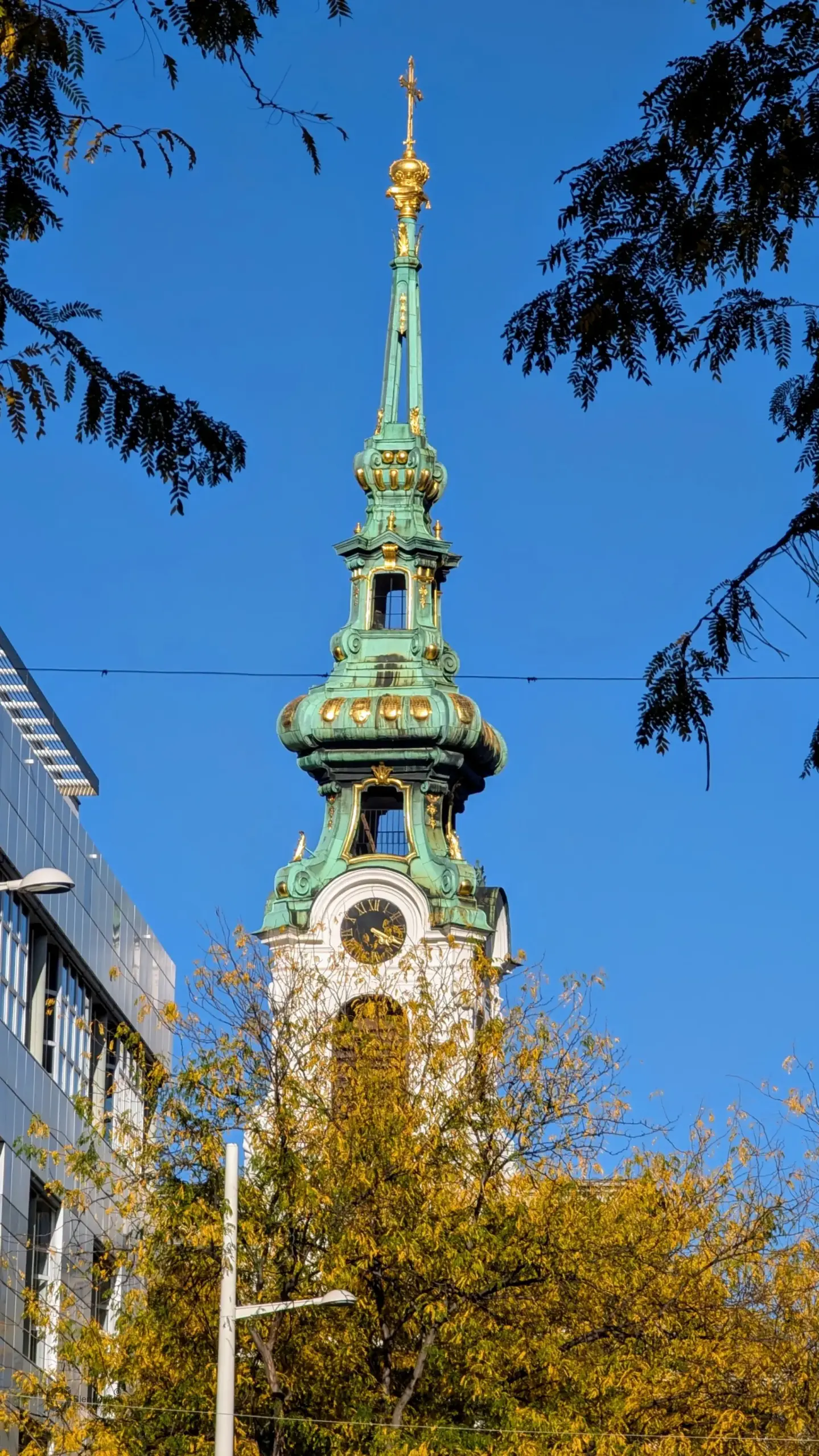 Nahaufnahme des barocken Kirchturms der Stiftskirche Wien an der Mariahilfer Straße vor strahlend blauem Himmel.
