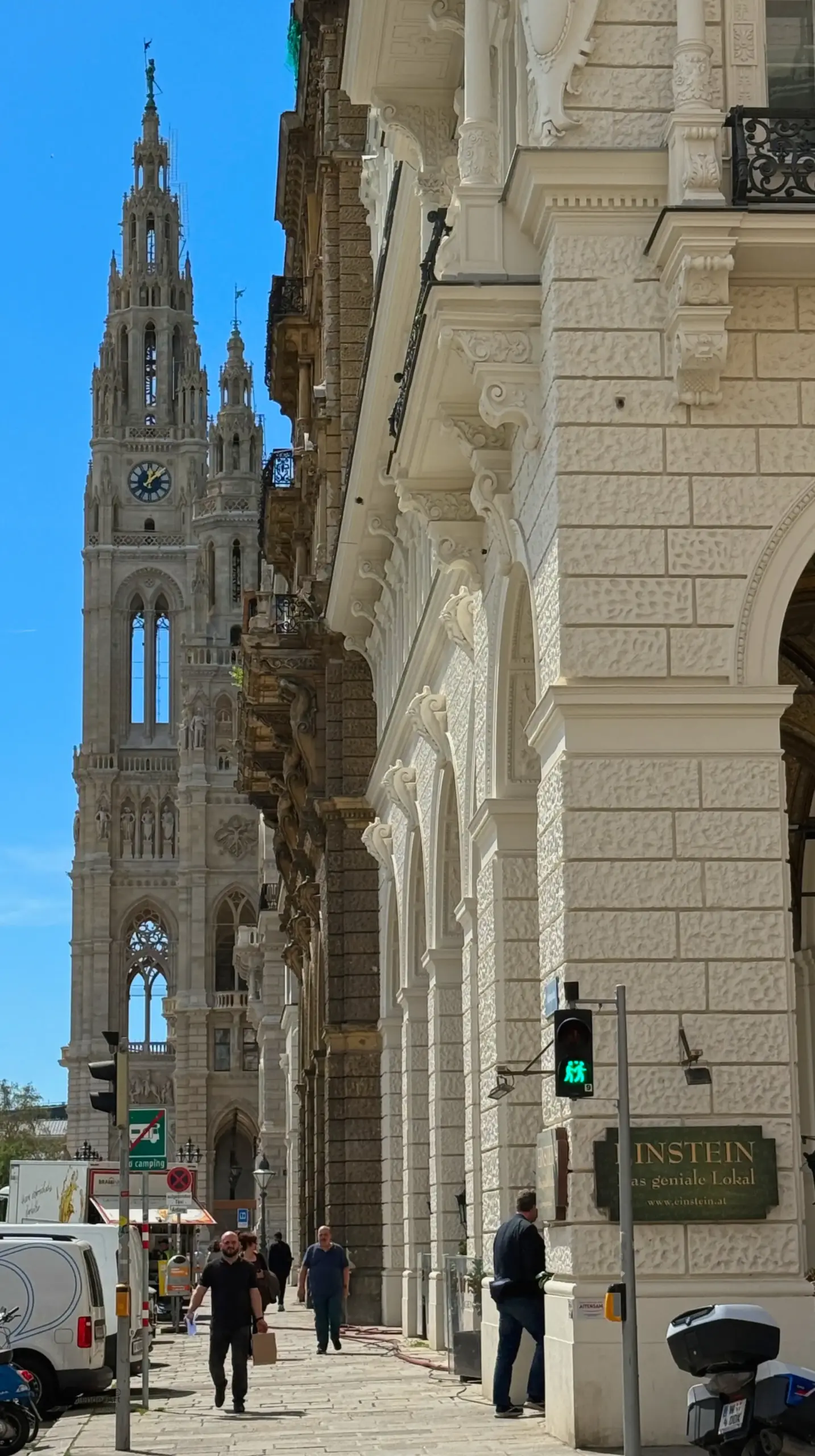 Seitenansicht des Wiener Rathausturms hinter einer hellen Steinfassade an der Ringstraße unter blauem Himmel.