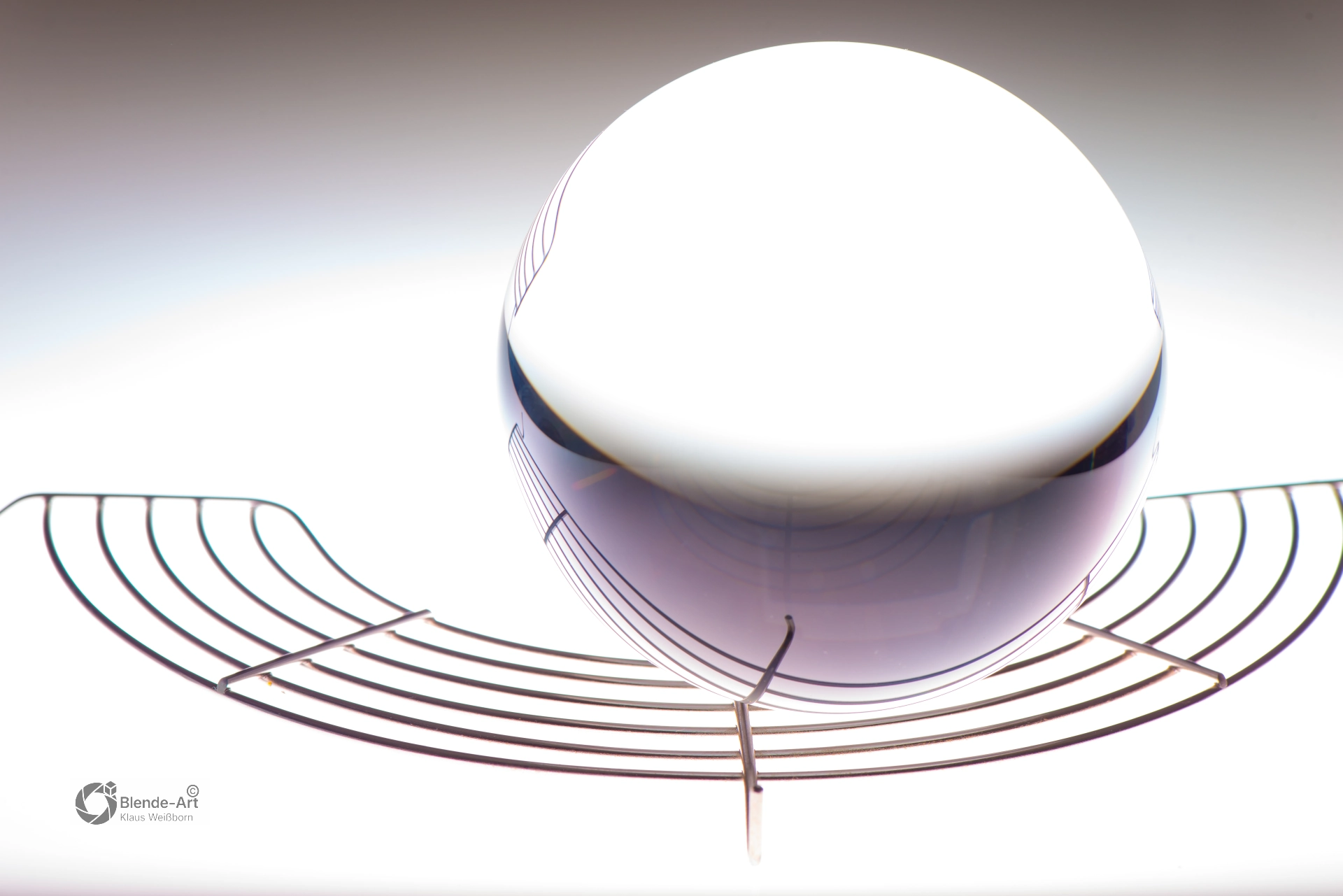 Glaskugel auf hellem Hintergrund mit feinen Linien, die sich symmetrisch unter der Kugel bogenförmig ausbreiten