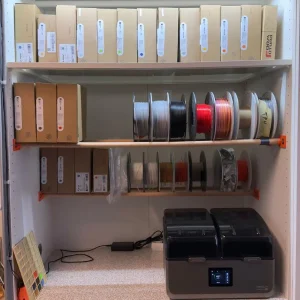 Schrank mit 3D-gedruckten Filamentrollenhaltern und Rundholzstangen zur übersichtlichen Aufbewahrung von 3D-Druck Filamentrollen