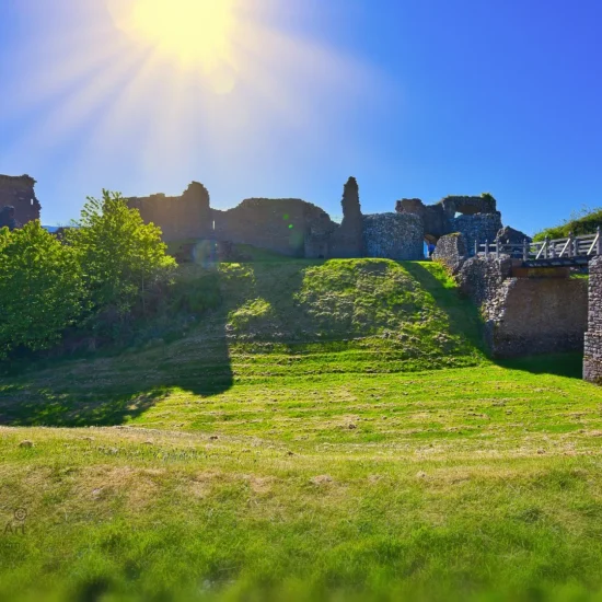 Ruine von Urquhart Castle bei Sonnenschein mit Burgmauer, Grünfläche und strahlendem Himmel über Loch Ness.