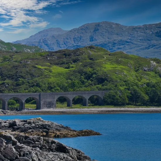 Loch nan Uamh Viadukt an der Westküste Schottlands mit Bergen im Hintergrund und Meeresbucht im Vordergrund.