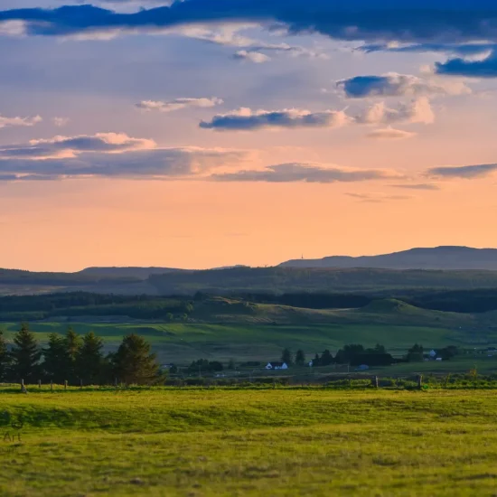 Abendliche Hügellandschaft auf der Isle of Skye mit orange-violettem Himmel und sattgrünen Weiden im Vordergrund.
