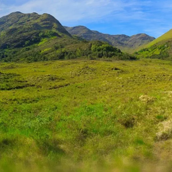 Weite Highland-Landschaft mit Wiesen, Bergen und Wald bei Kinloch Hourn in Schottland.