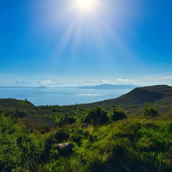 Sonnenüberflutetes Panorama auf der Isle of Skye mit Blick über grüne Hügel und das schimmernde Meer, aufgenommen auf dem Weg zum Old Man of Storr.